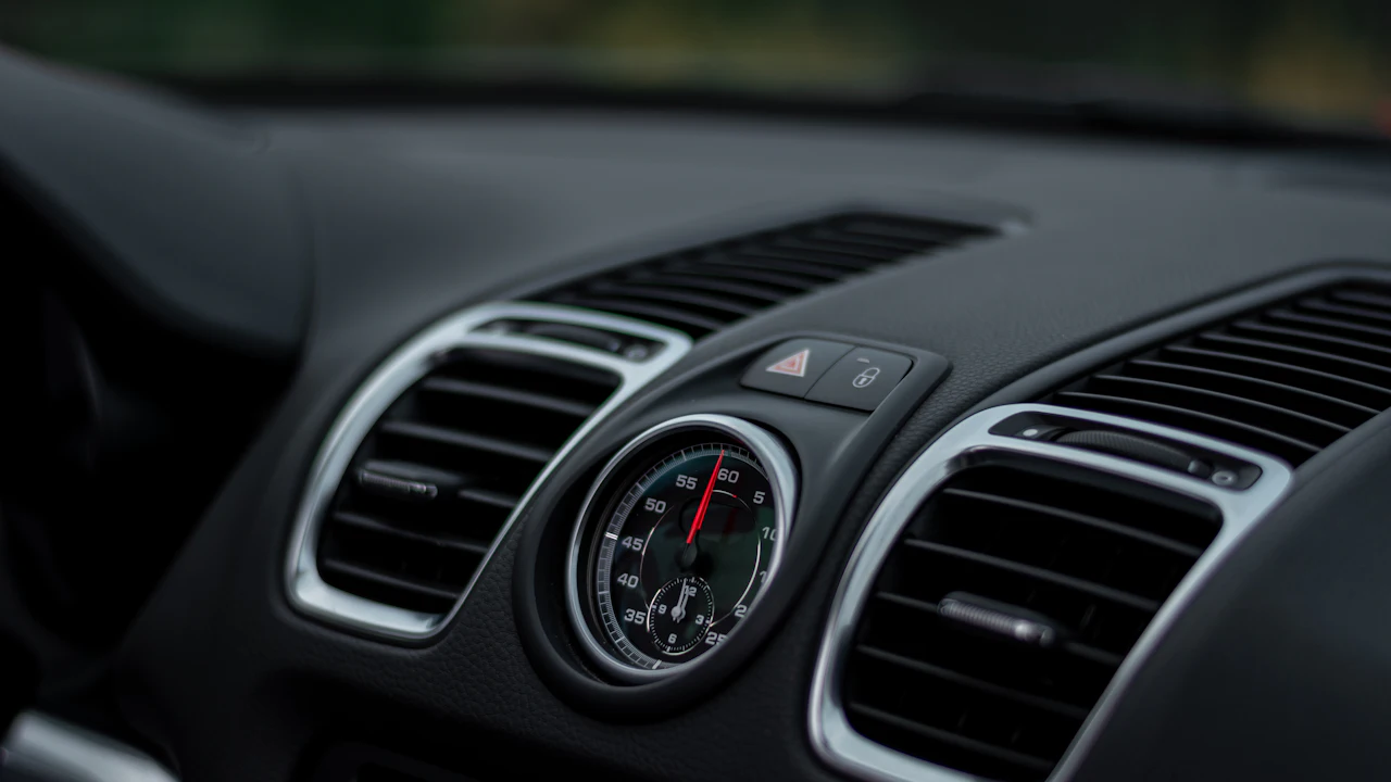 A car dashboard photographed close up showing the centre air vents and a small analogue clock