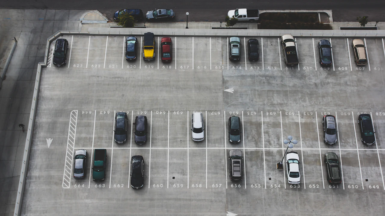 An overhead view of a car park, rows of vehicles standing in bays with numbers painted on the tarmac