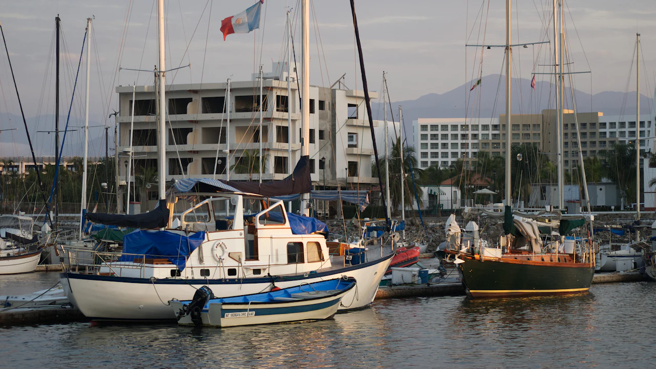 Sailing boats and small motor cruisers moored side by side in a marina at dusk, masts crowding the skyline in front of low white buildings