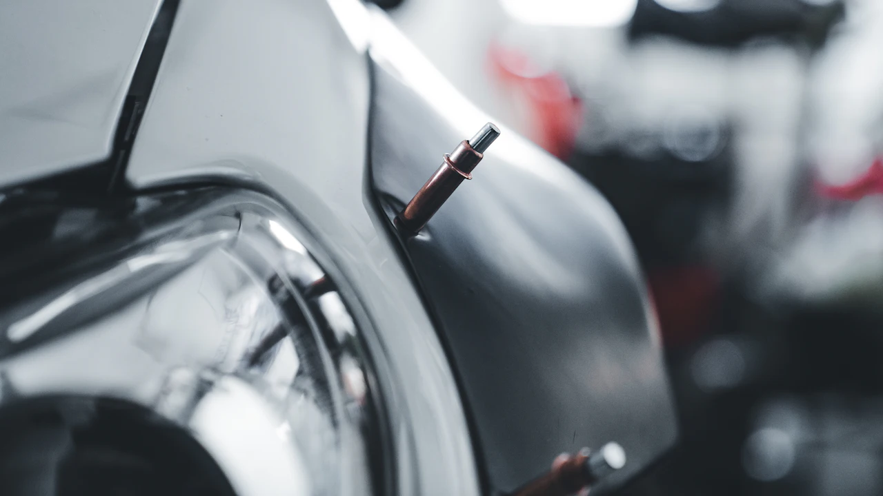 A car’s front wing panel pulled away from the headlight with a body tool in the gap