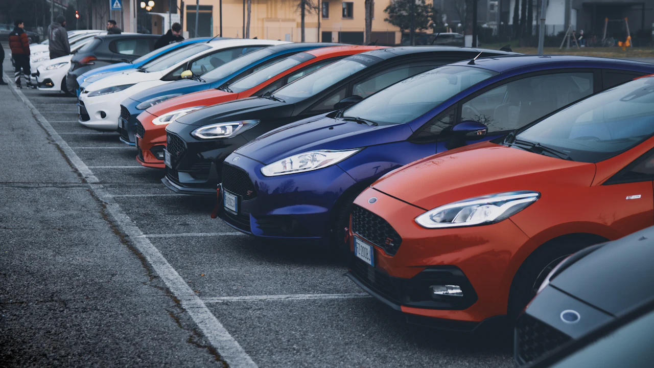 A row of small used hatchbacks in various colors lined up in a parking lot