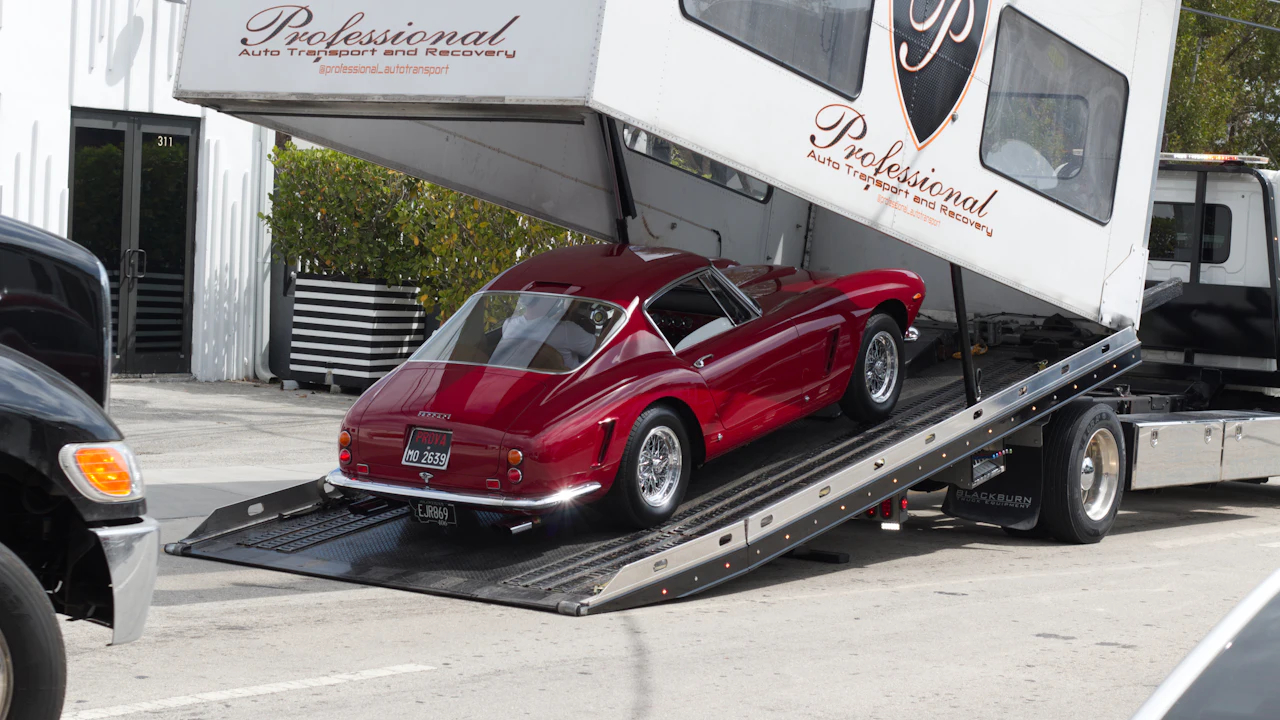 A dark red classic coupe being loaded up the ramps of a flatbed vehicle transporter outside a recovery company’s unit