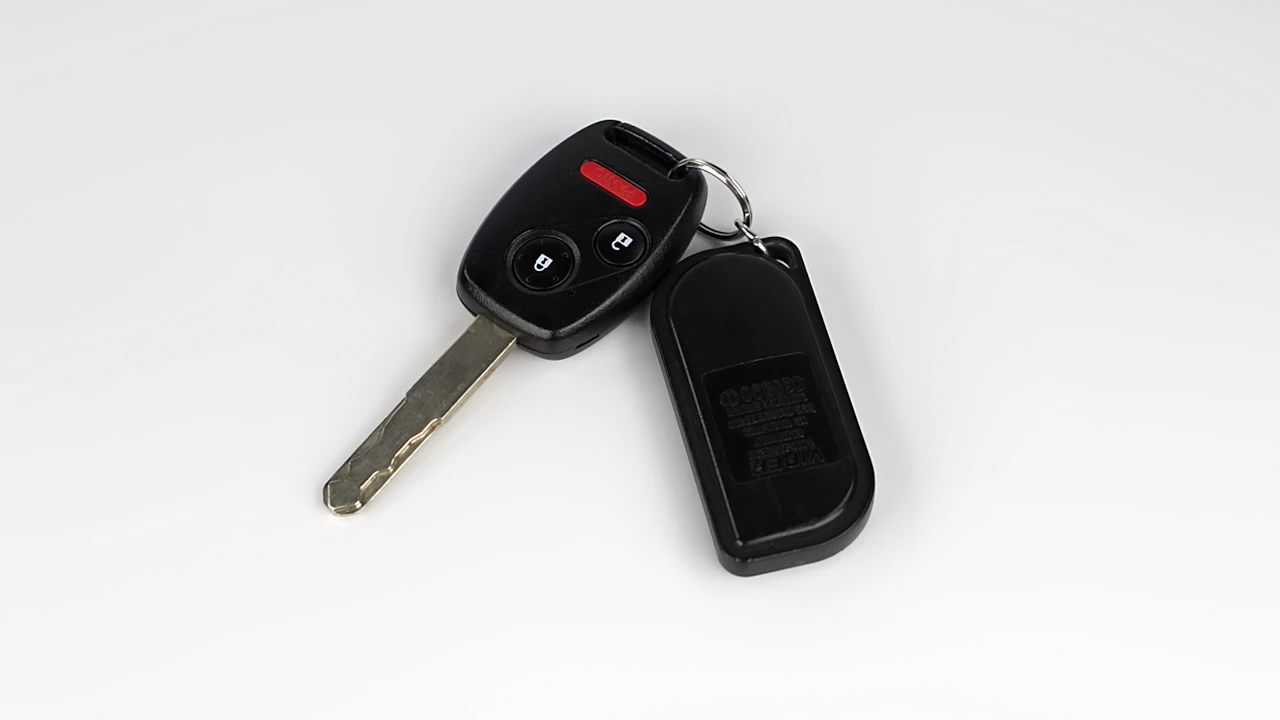 A black car key with an integrated remote lying next to its plastic fob on a plain white surface