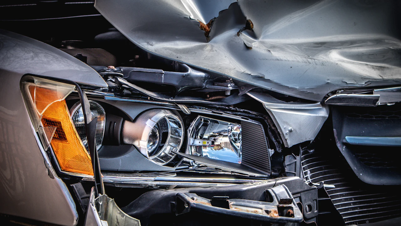 A damaged silver car with a crushed hood and broken headlight assembly