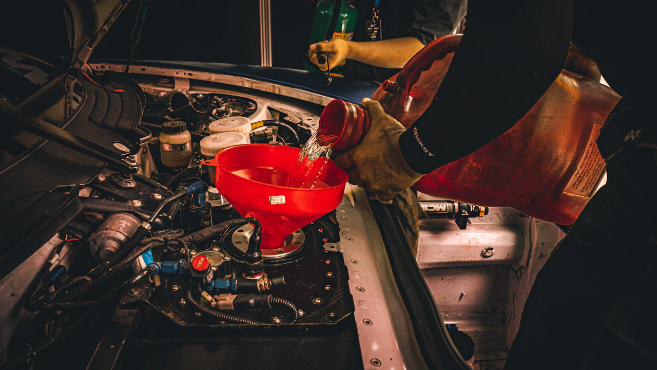Fresh oil being poured through a red funnel into an engine, gloved hands holding the bottle