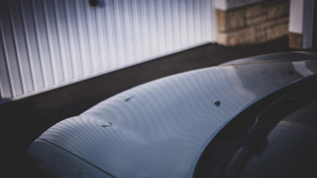 A car panel in low light covered with shallow round dents, the reflections in the paint breaking across each one