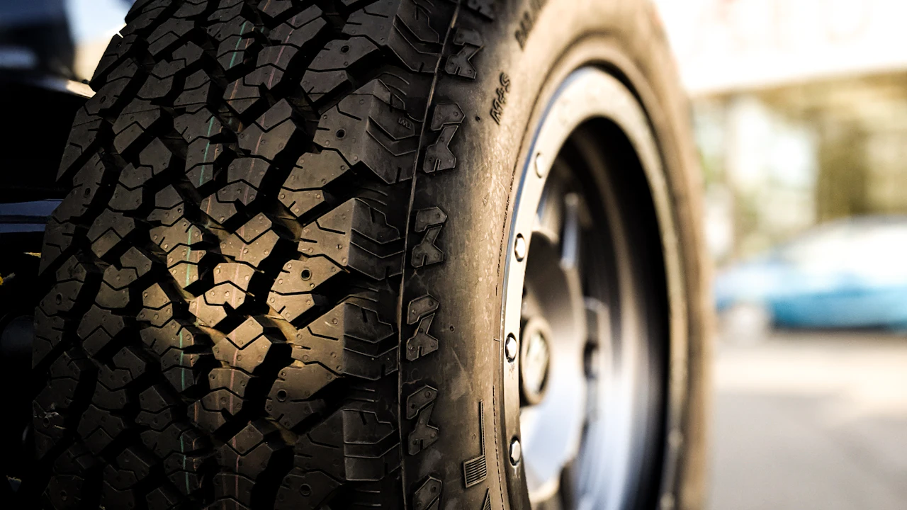 A close-up of a car wheel and tyre photographed from the side, the tread blocks and sidewall lettering in sharp focus