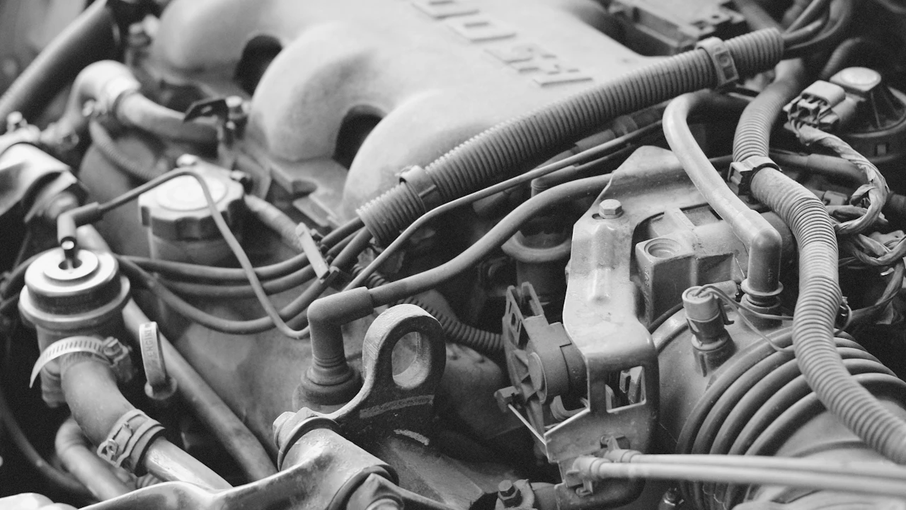 A dense engine bay in black and white, filling the frame with an intake manifold, plug leads, vacuum hoses, a wiring loom and hose clamps