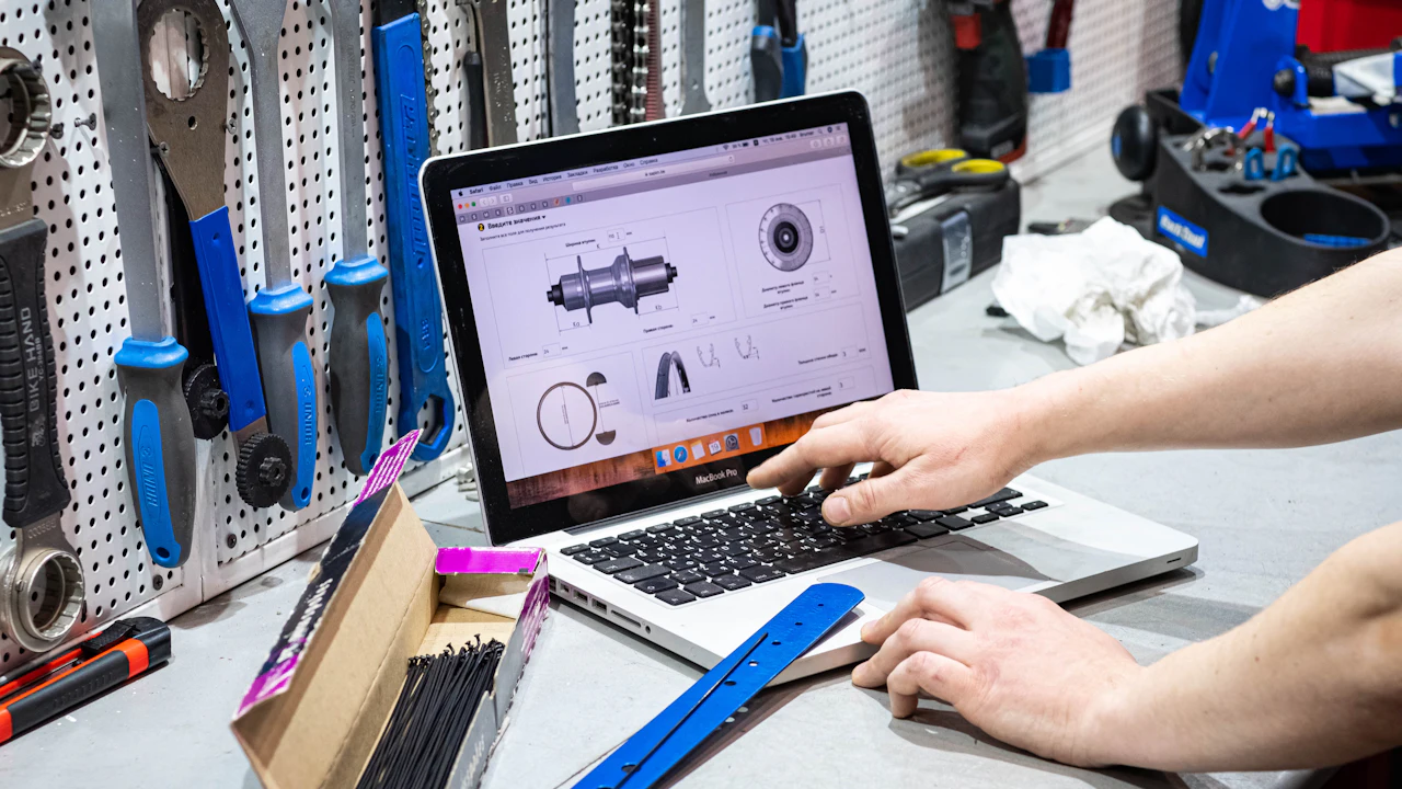 A laptop on a workbench showing a technical parts drawing, hands at the keyboard