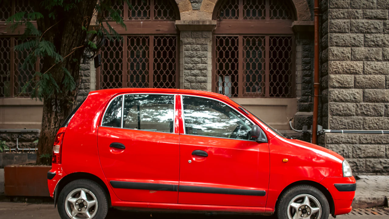 A red car is parked beside a stone building