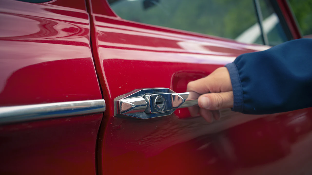 A person’s hand on the painted door panel of a red car