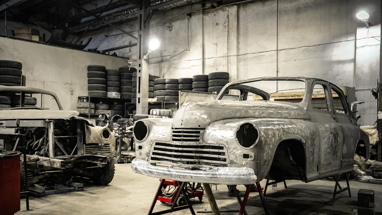Several bare-metal classic car bodyshells standing on trestles in a restoration workshop under strip lighting