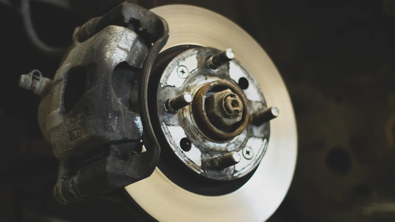 A close-up of a brake caliper and wheel hub with the road wheel removed, the studs and disc face lit from the side