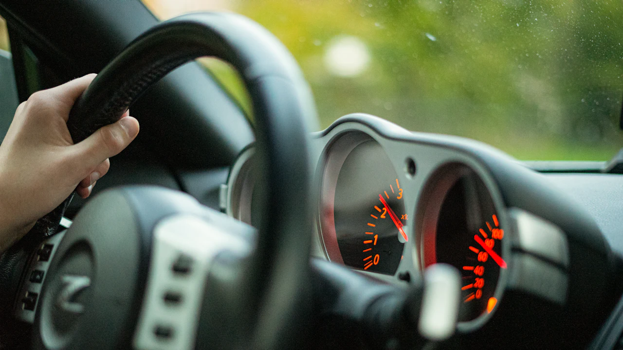 A driver’s hands resting on a steering wheel with the instrument cluster lit behind it