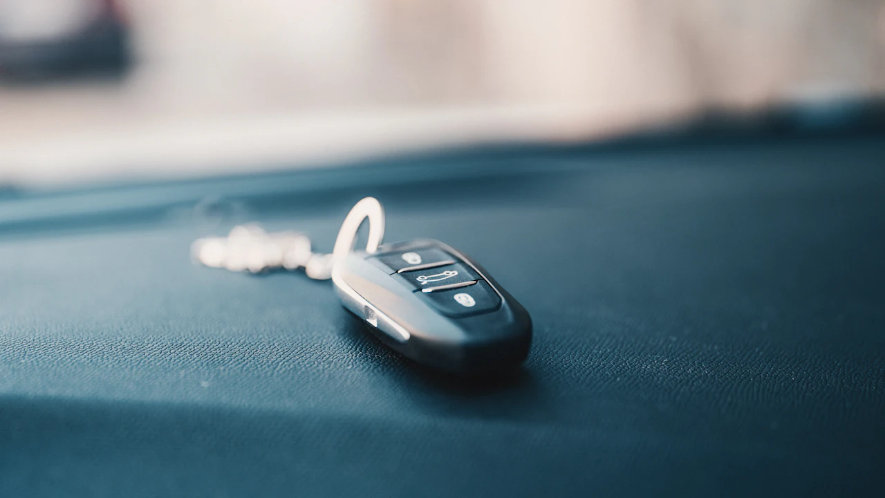 A black flip key fob on a white beaded keyring, lying on a dark teal car interior surface