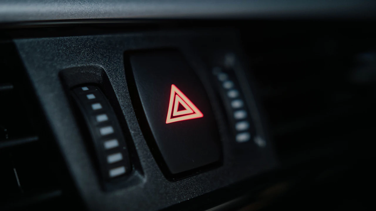 A hazard warning light switch lit red on a dark dashboard