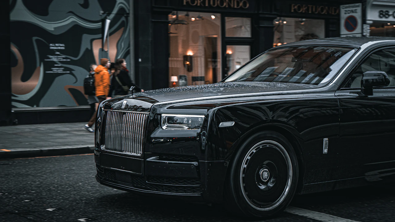 A black Rolls-Royce saloon parked on a wet city street, front three-quarter view showing the upright grille