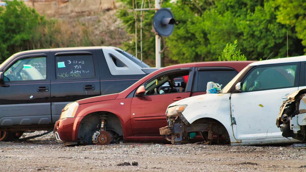 Three crash-damaged cars with wheels removed, parked on gravel in a salvage yard