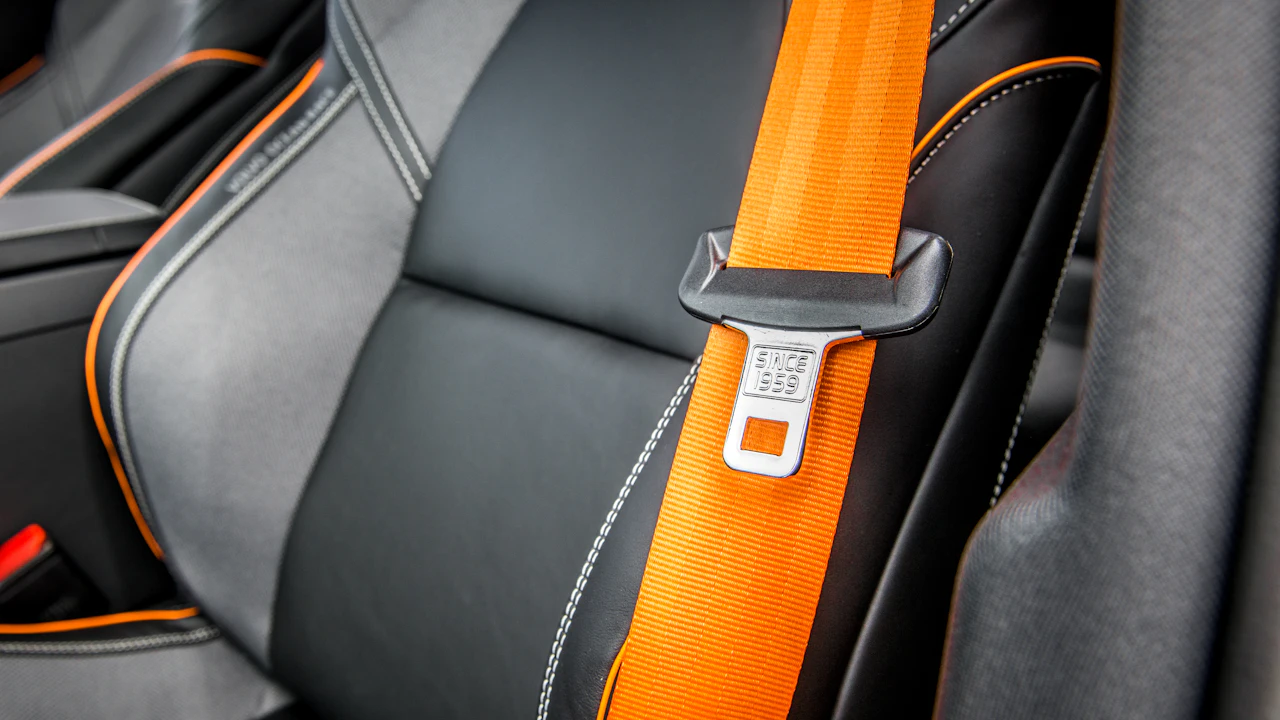 An orange seatbelt fastened across a black sports seat
