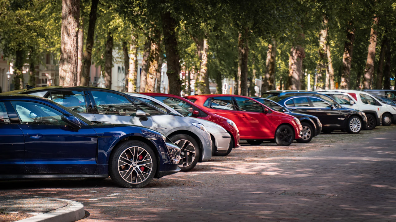 A blue and a red car parked on a road in daylight, seen from the front three-quarter angle