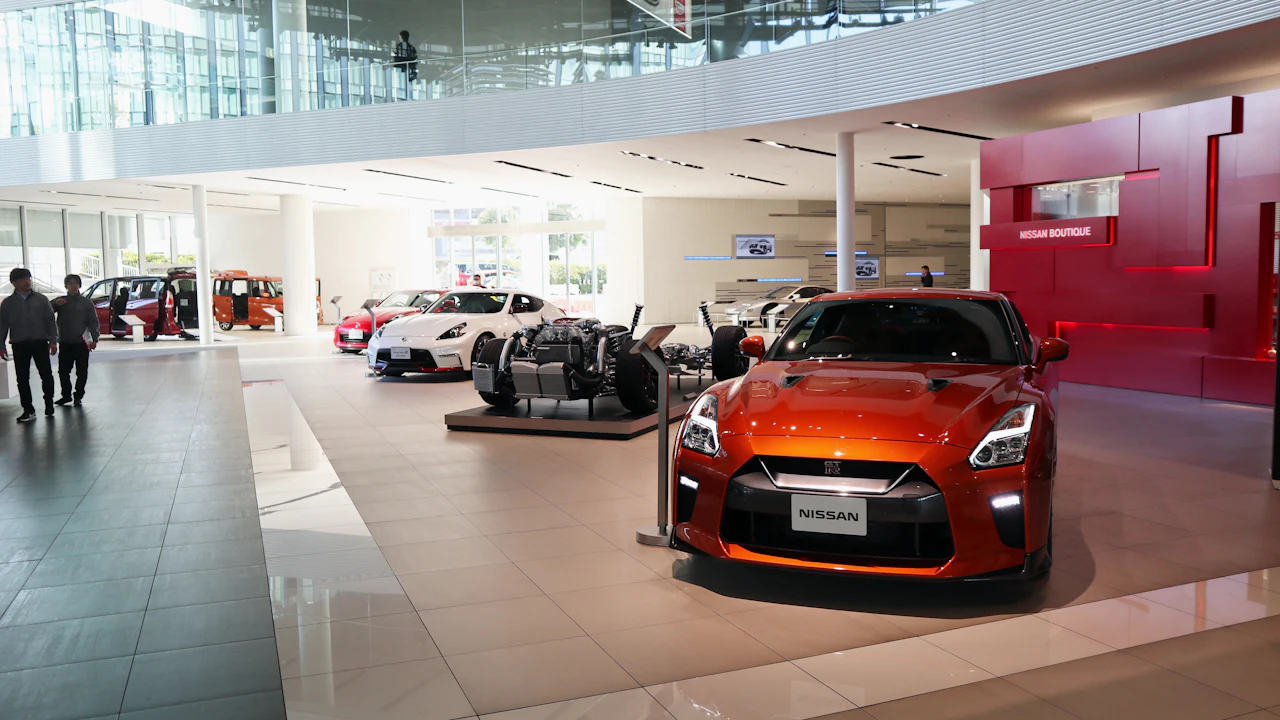 The floor of a car showroom, a red sports car in the foreground under bright lighting