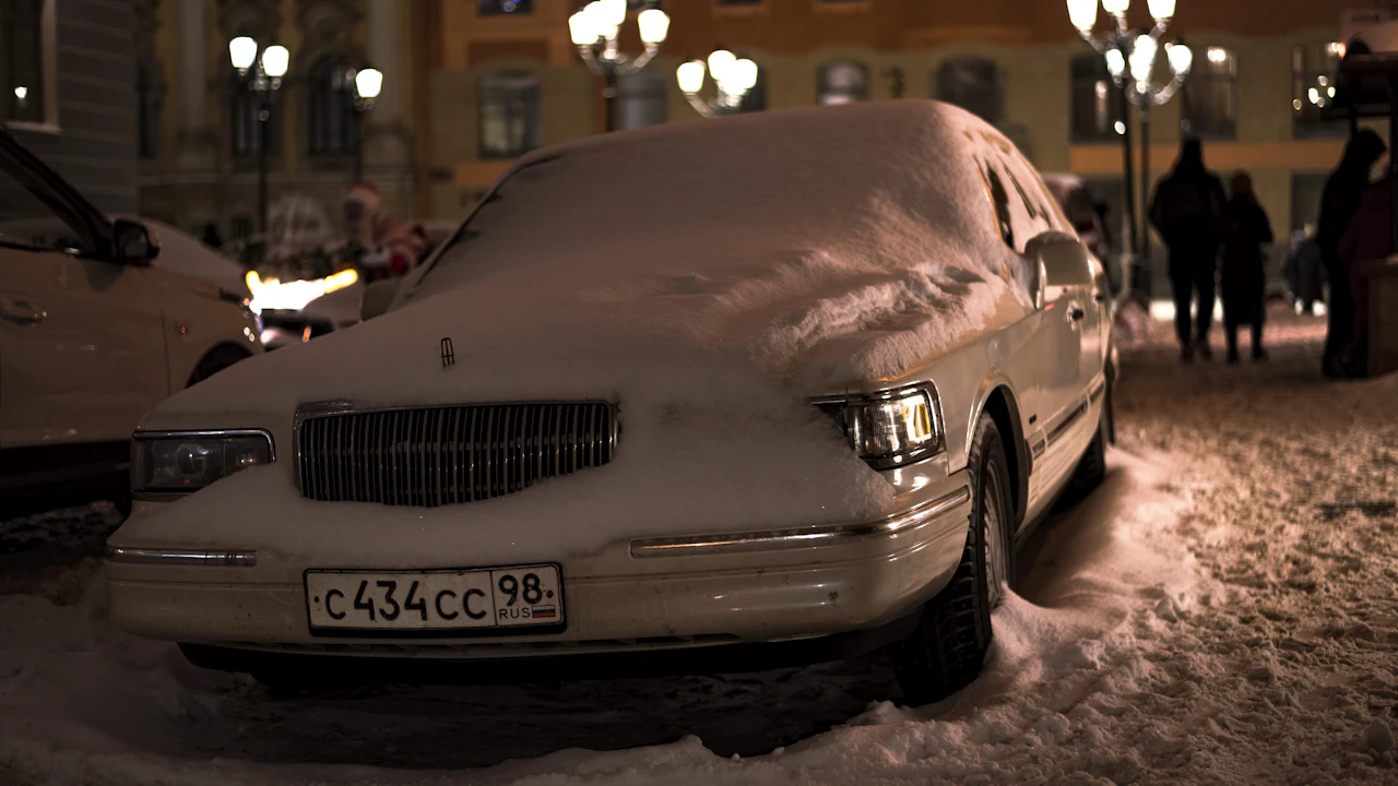 A car buried under snow at night on a lamplit street