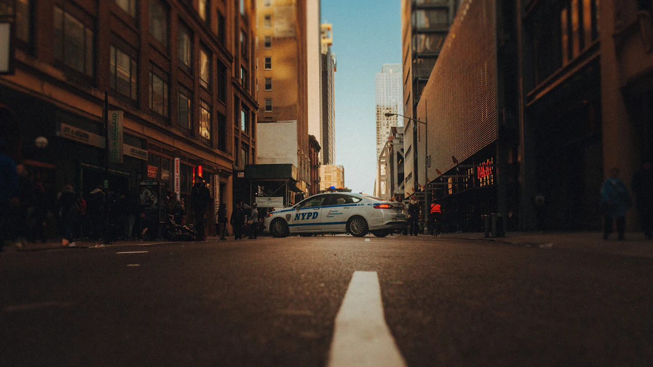 A near-empty city street at dusk between tall buildings, with a single pale car parked in the distance