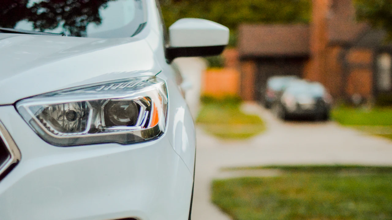 The front corner and headlight of a white SUV parked on a residential driveway