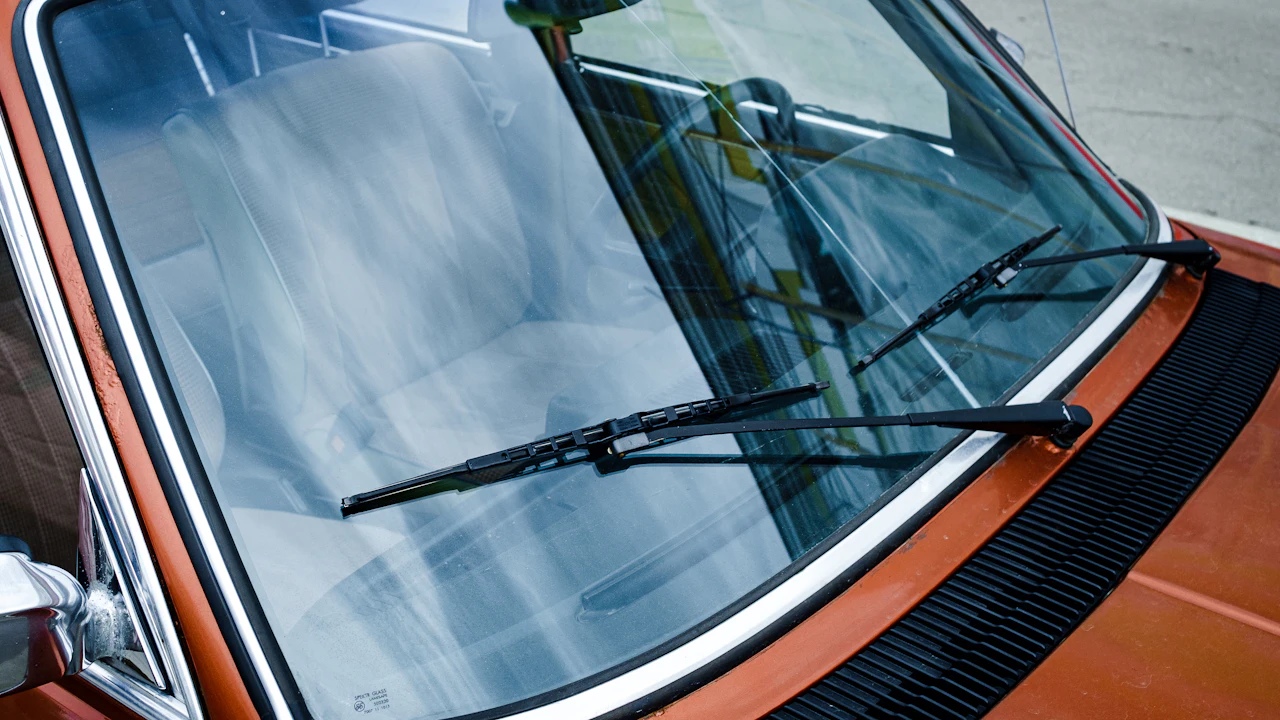 The windscreen of an orange car seen from outside, wipers and dashboard visible through the glass