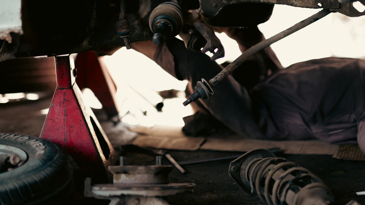 A mechanic working underneath a raised vehicle, reaching up into the underside of the car