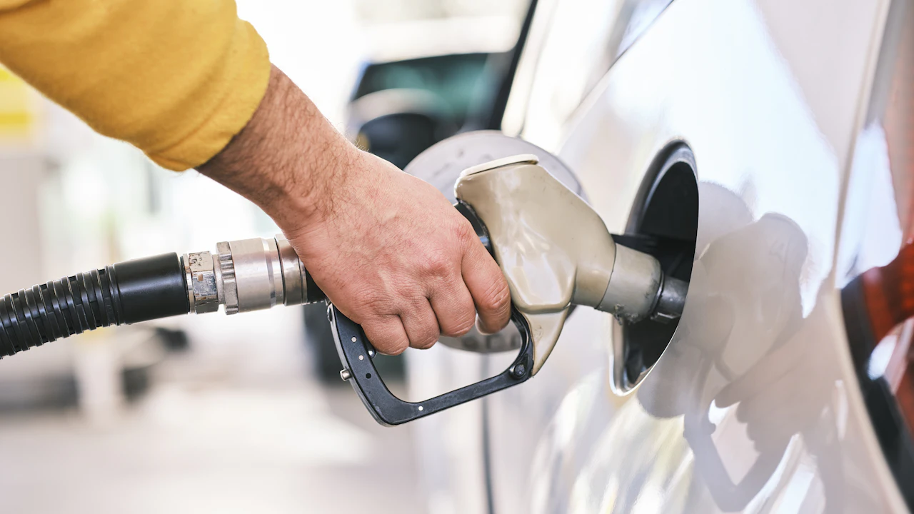 A hand holding a fuel nozzle in the filler neck of a white car